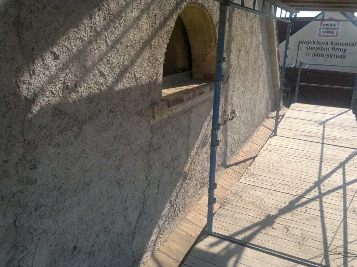 Nová hrubá omítka na zdi varny, klenutý otvor, podlaha lešení.