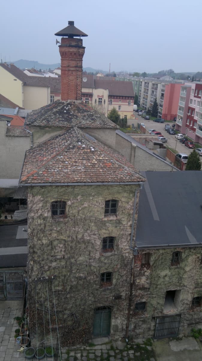Pohled z lešení na střechy sladovny a na komín hvozdu se stříškou.